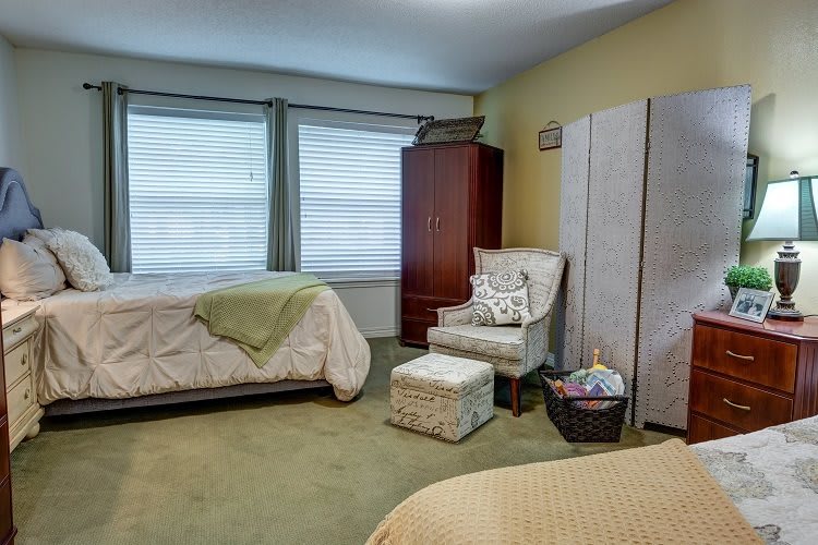 A cozy bedroom with two beds, a chair, and a cabinet near the window.