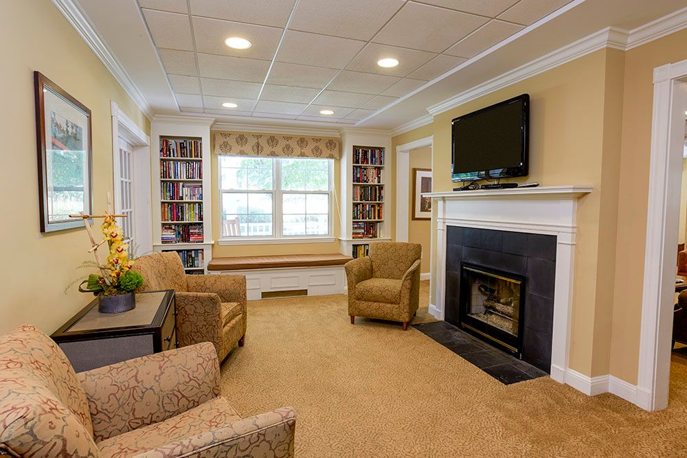 A cozy living room featuring a fireplace, television, armchairs, and bookshelves with a window seat.
