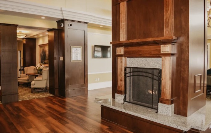 A cozy living room with a classic wooden fireplace and polished wooden flooring.