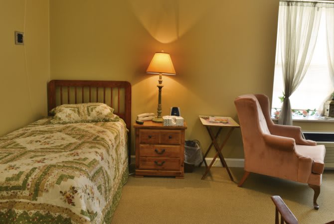 A cozy bedroom with a bed, nightstand, lamp, and chair.