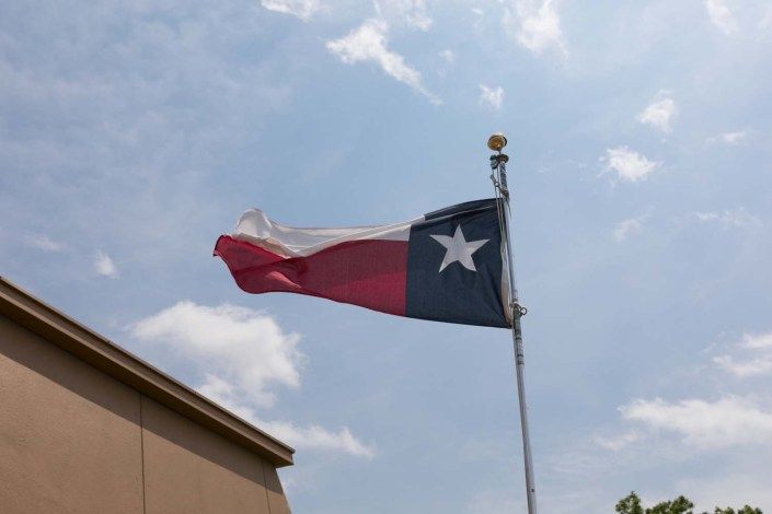 A Texas flag waving on a pole against a cloudy sky.
