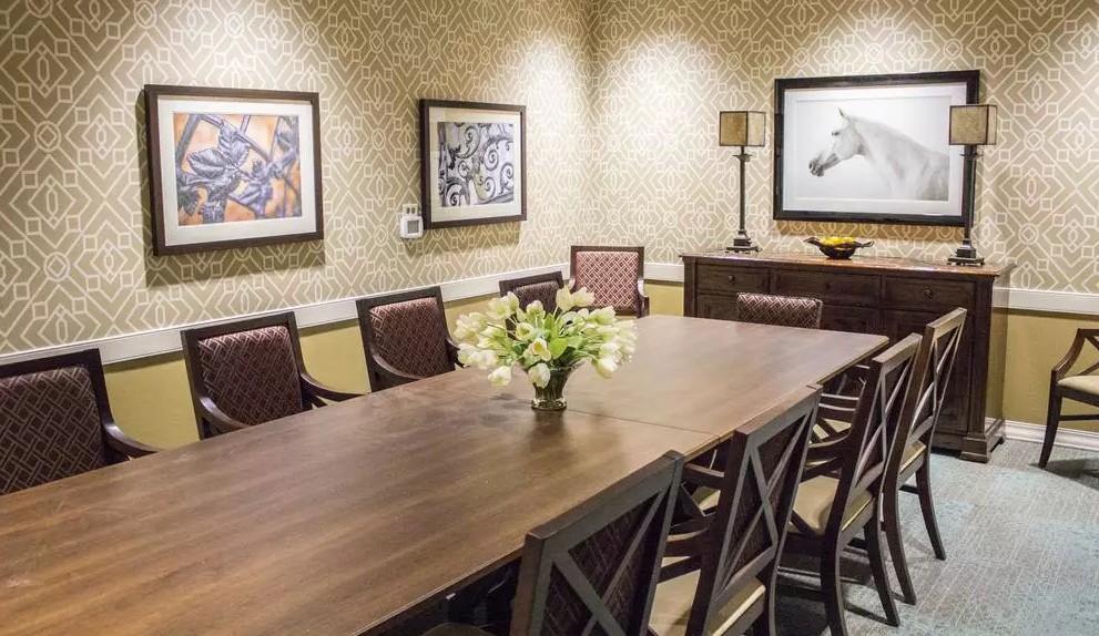 A well-decorated conference room featuring a large meeting table surrounded by chairs, with artwork on the walls and a decorative lamp.