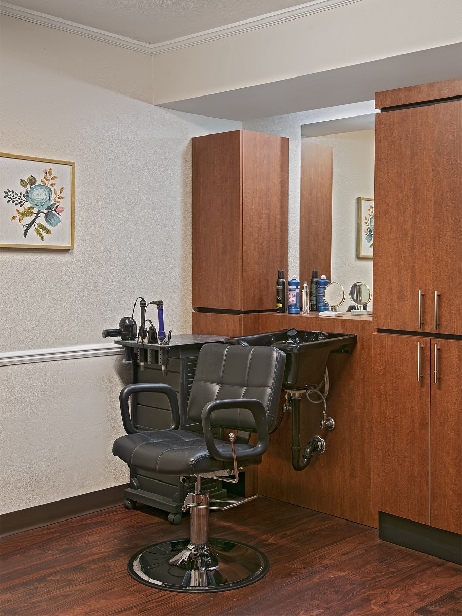 An interior view of a hair salon featuring a barber chair, wooden cabinets, and a mirror.
