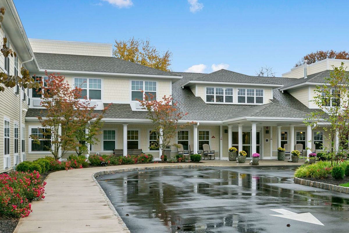 A two-story residential building with a pond and trees in the foreground.