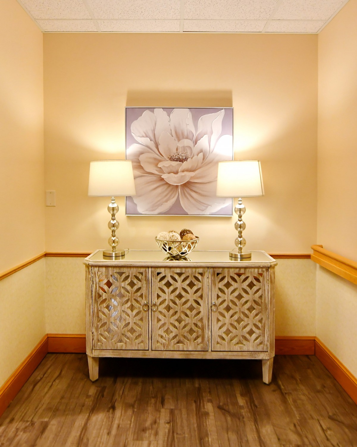 A stylish hallway featuring a decorative console table with two lamps and a large flower painting above.