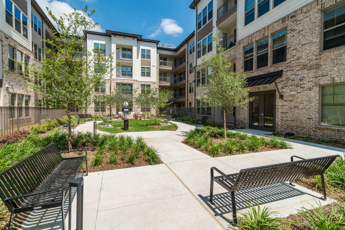 A modern apartment complex with a landscaped courtyard featuring benches and trees.