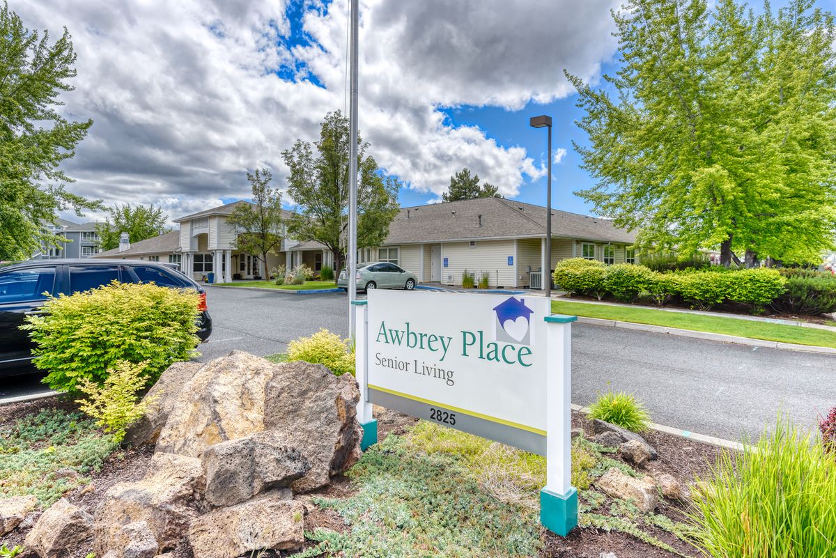 A sign for Aubrey Place Senior Living in front of a residential building on a cloudy day.