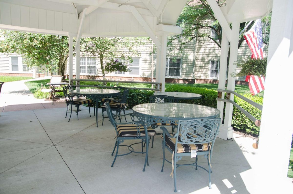 A cozy outdoor gazebo with tables and chairs surrounded by lush greenery.