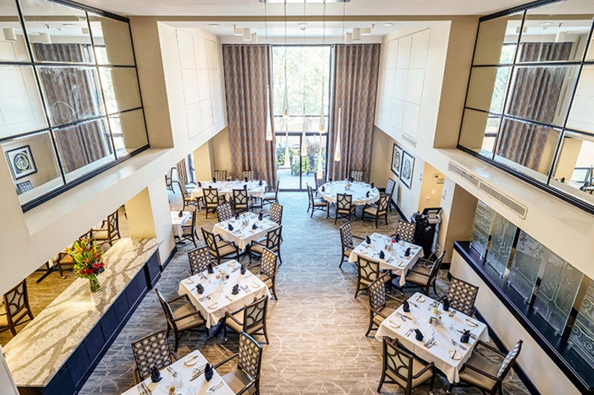 A spacious and elegantly designed restaurant dining area with neatly arranged tables and chairs, featuring large windows with curtains.