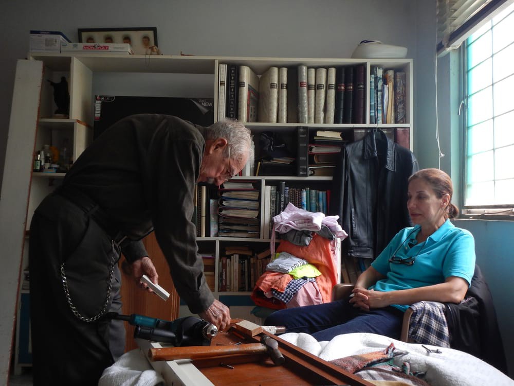 An elderly man and a woman engage in conversation in a room with bookshelves.