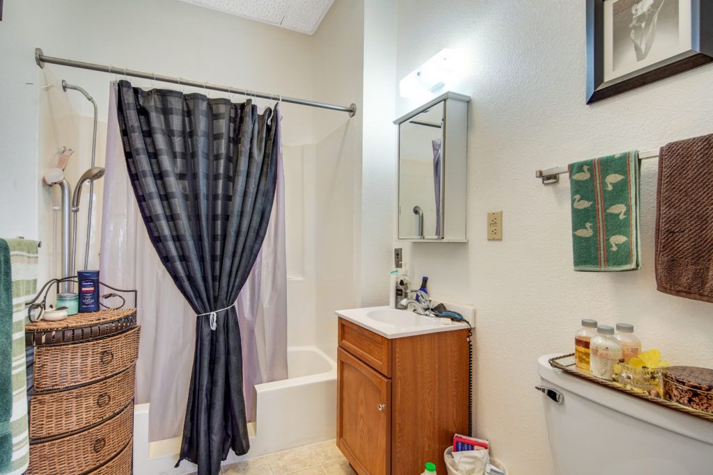 A small bathroom featuring a sink with a wooden cabinet, a mirror above, and a shower with a dark curtain.