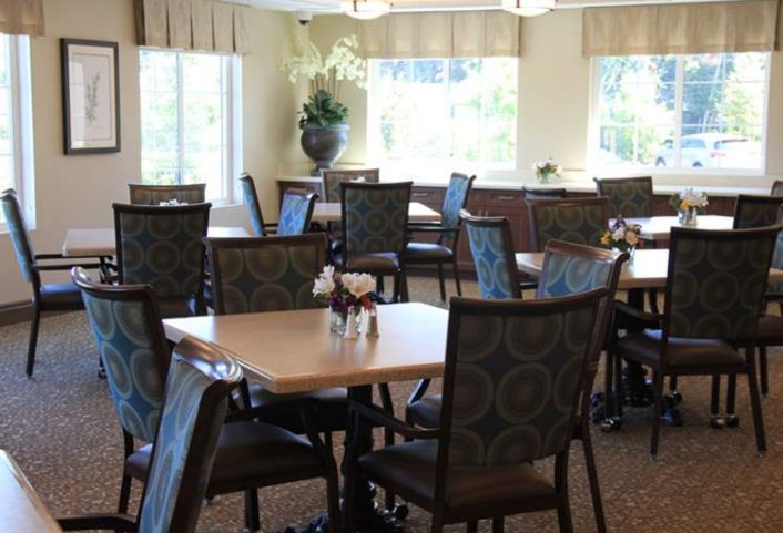 An empty dining room with neatly arranged tables and chairs, illuminated by natural light from large windows.