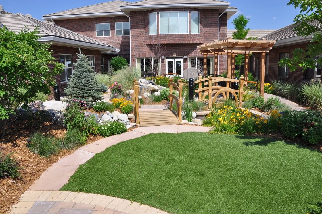 A beautifully landscaped garden with a lush lawn, pathway, and wooden bridge in front of a modern house.