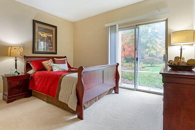 A cozy bedroom featuring a wooden sleigh bed with red bedding, adjacent to a sliding glass door overlooking a garden.