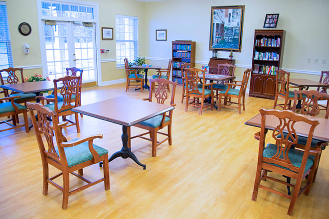 A bright community room with tables, chairs, and bookshelves.