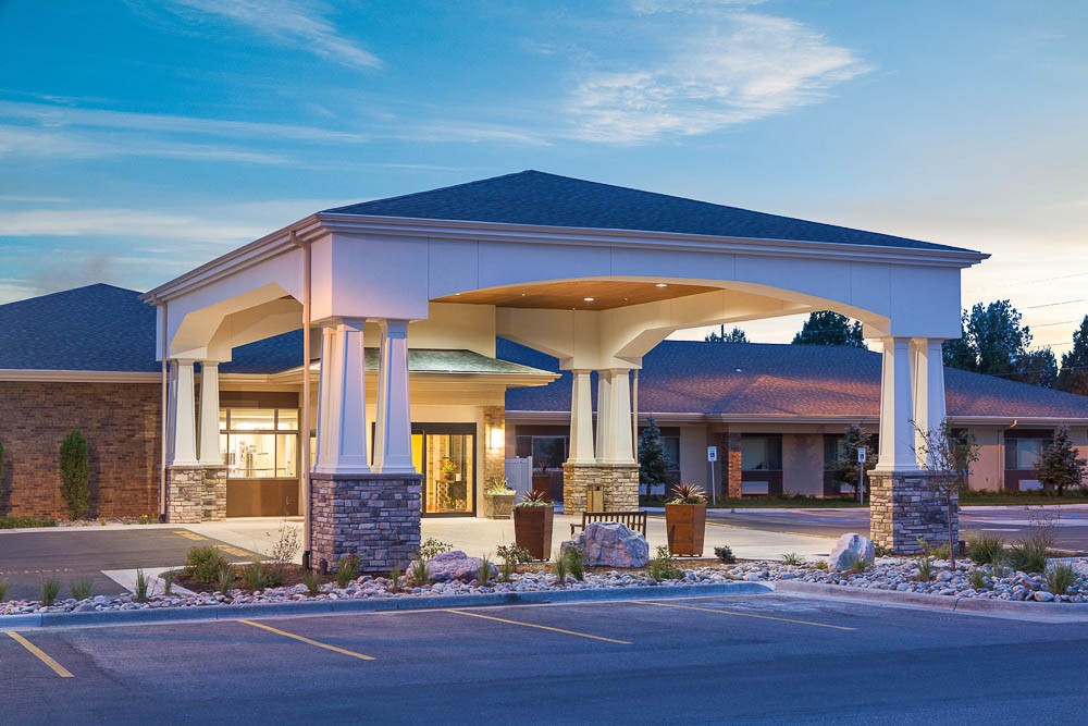 A building with a covered entrance featuring columns and a landscaped area, set against an evening sky.