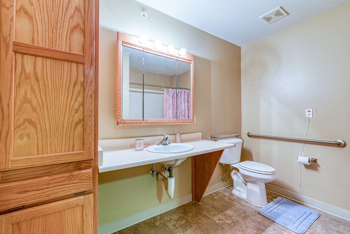 A clean and spacious bathroom with a large mirror, sink, toilet, and shower area.