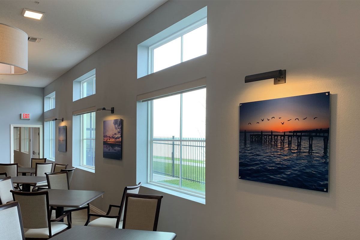 A modern interior space featuring large windows and wall art, with tables and chairs arranged nearby.