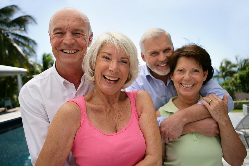 A group of four smiling seniors enjoying time together outdoors.