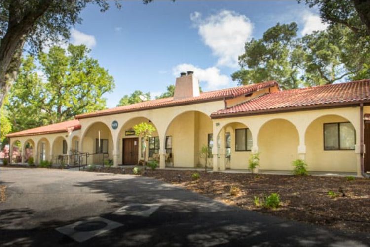 A charming Spanish-style house with prominent arches and a terracotta roof, surrounded by trees.