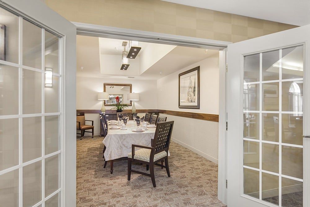 A well-decorated dining room with a set table and elegant chairs, viewed through open French doors.