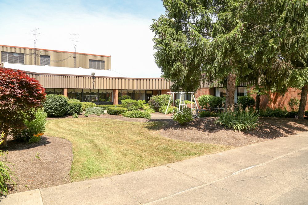 A view of a modern building surrounded by well-maintained greenery and a sidewalk.