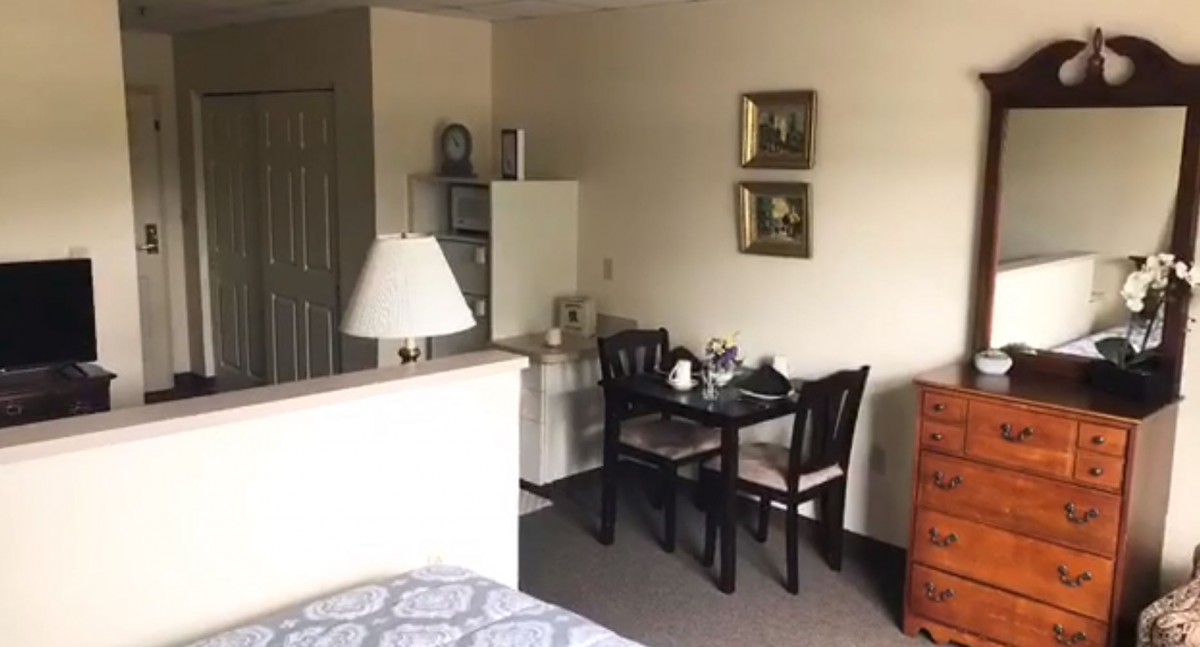 A cozy apartment with a small dining area featuring a table and chairs, adjacent to a lamp and decorated with framed paintings.