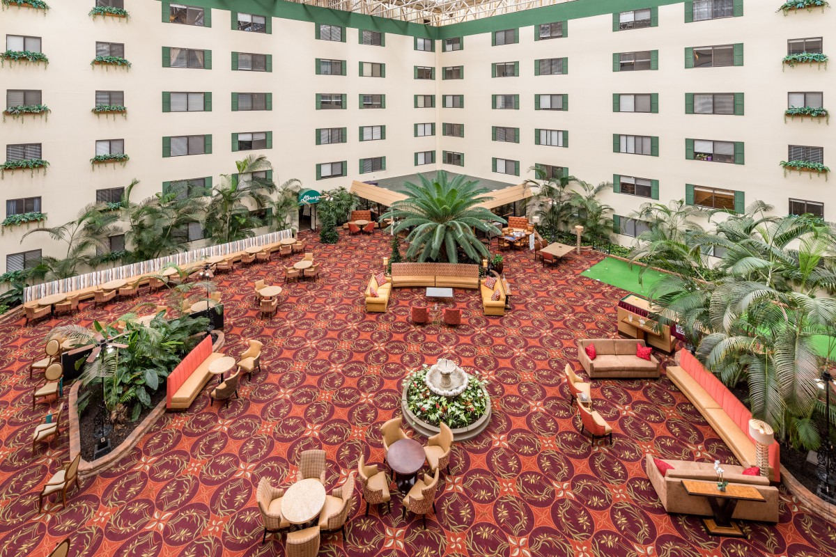 A spacious hotel atrium featuring a vibrant carpet, multiple seating areas, and lush green plants.