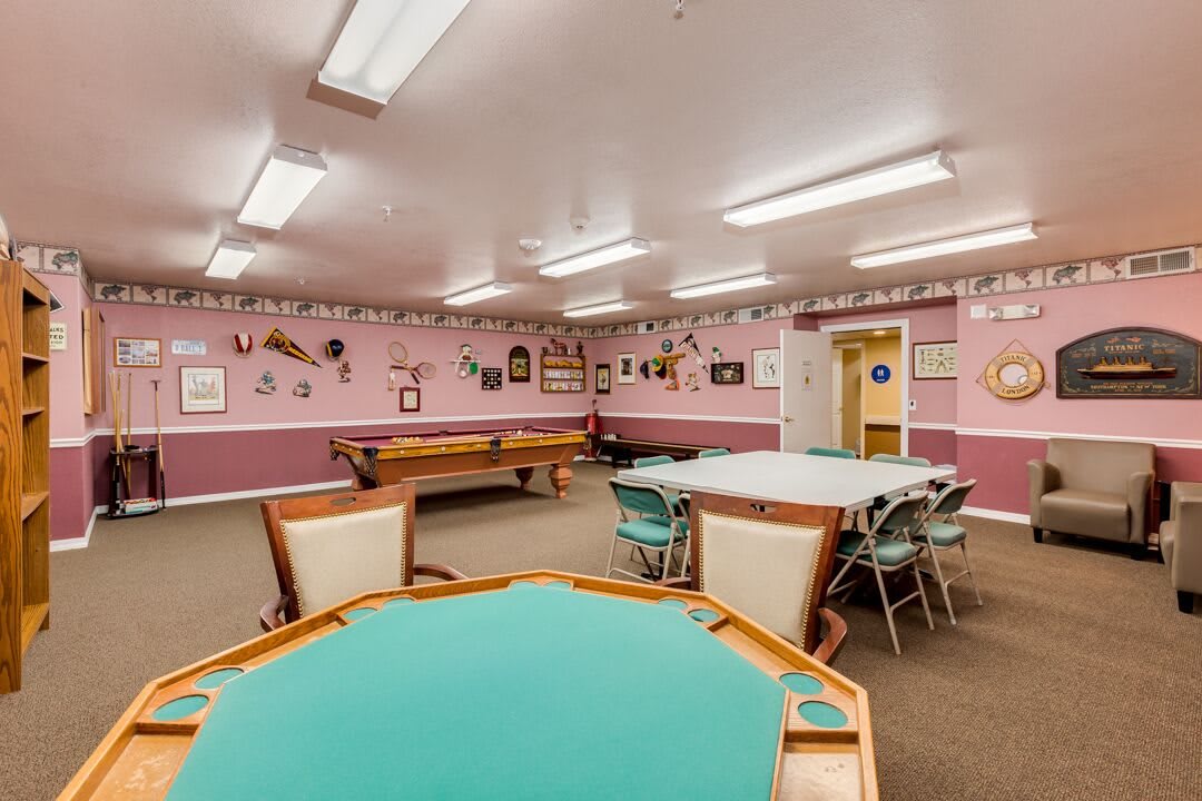 A spacious game room featuring a pool table and card tables, with pink walls adorned with various decorations.