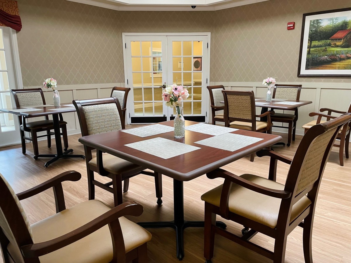 A cozy dining area with neatly arranged tables and chairs, featuring a vase of flowers as a centerpiece.