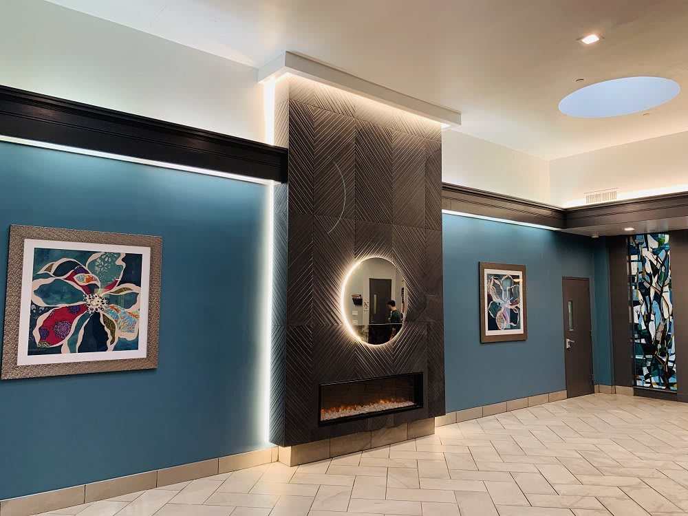 A modern lobby with blue walls, featuring abstract artwork and a central illuminated mirror.