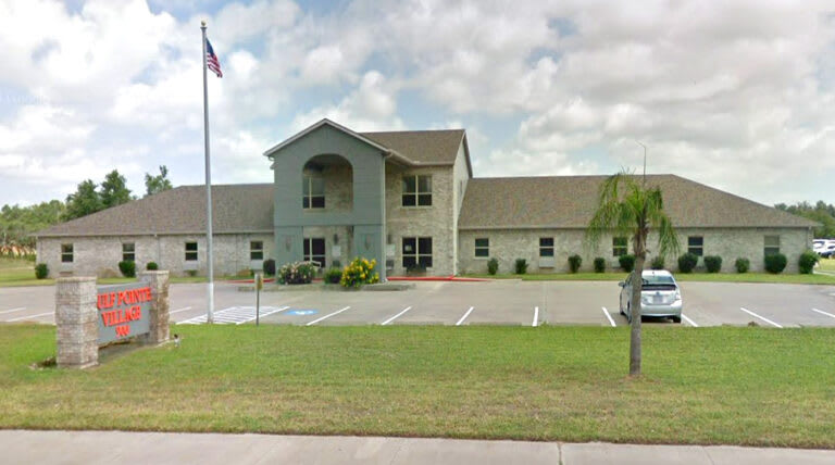 A building with a flagpole, surrounded by a parking lot and well-maintained lawn.