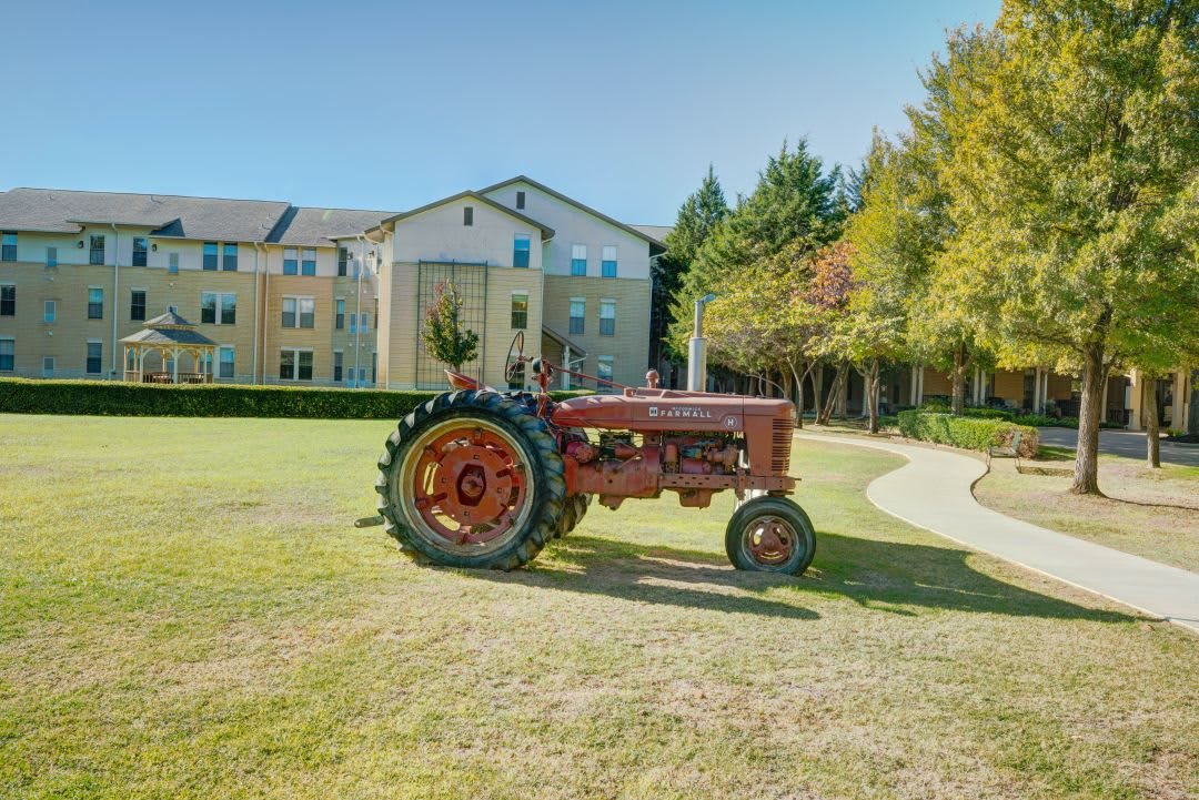 An old tractor parked on a grassy area in front of a large building under a clear blue sky.