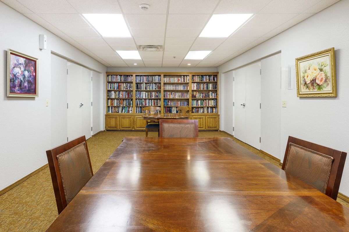 A conference room with a large wooden table surrounded by chairs, featuring bookshelves filled with books in the background.