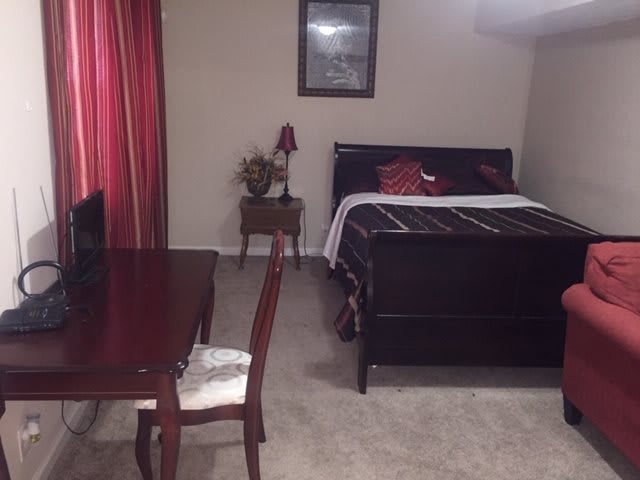 A cozy bedroom featuring a bed, a table with a chair, and a lamp next to the curtains.