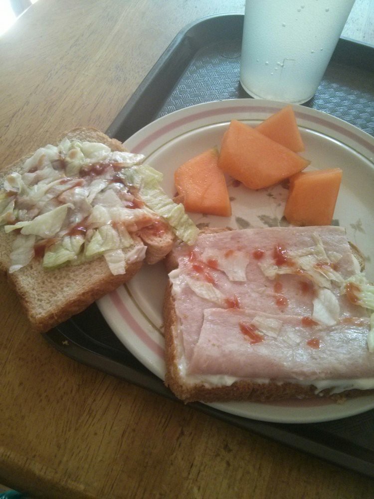 A meal featuring an open-faced sandwich with ham, lettuce, and mayonnaise, accompanied by slices of cantaloupe.
