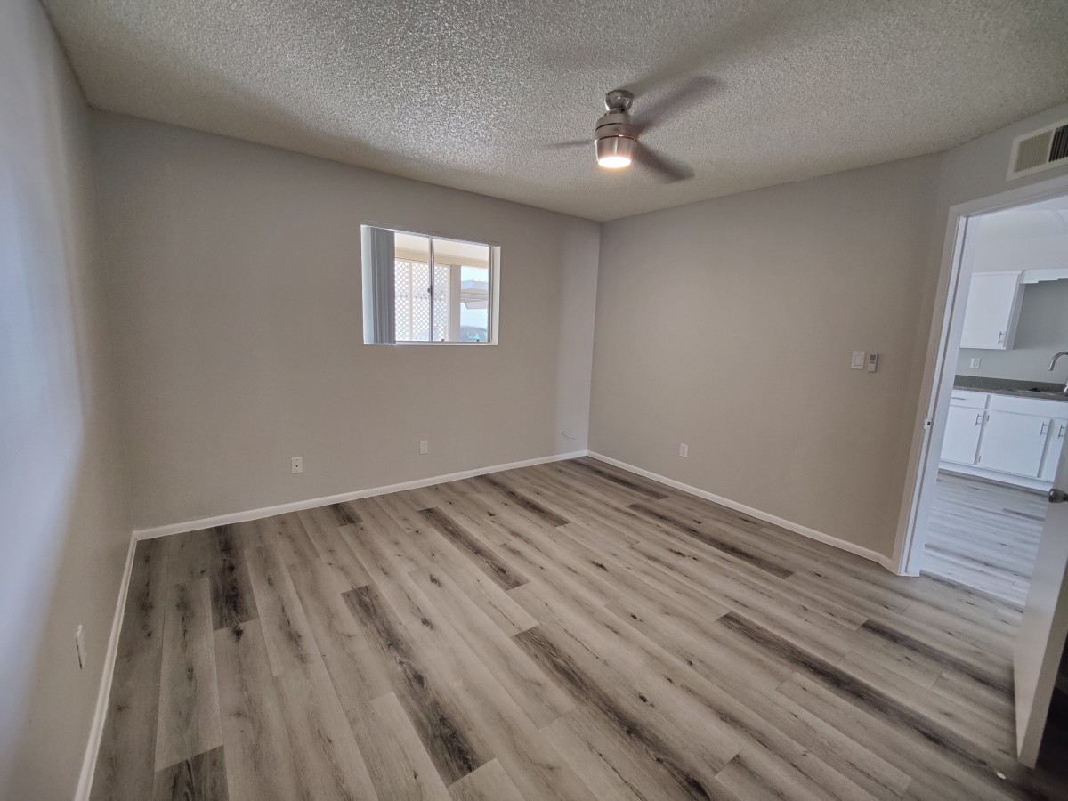 An empty room with wood flooring, gray walls, a ceiling fan, and a window.