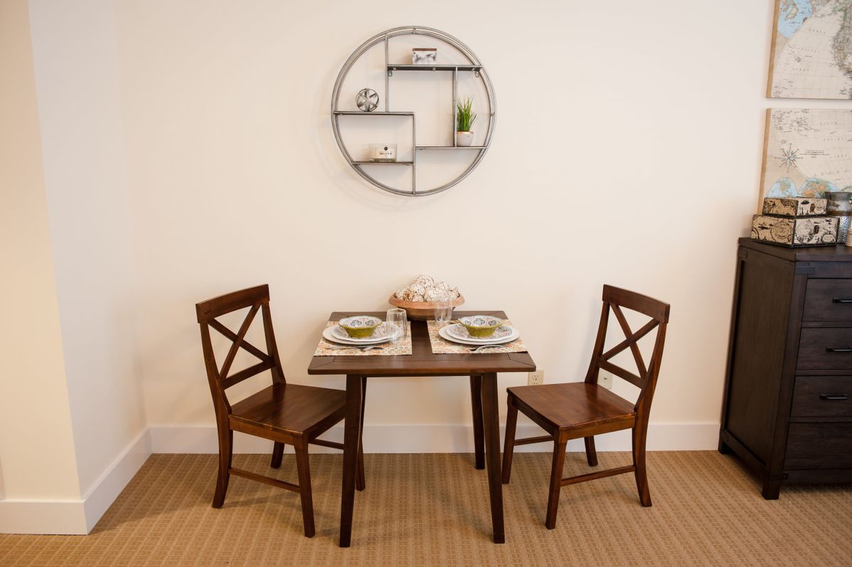A cozy dining area with a wooden table set for two, accompanied by matching chairs and complemented by a circular wall shelf.