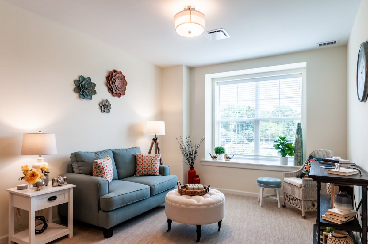 A cozy living room with a sofa, armchair, and bright window letting in natural light.