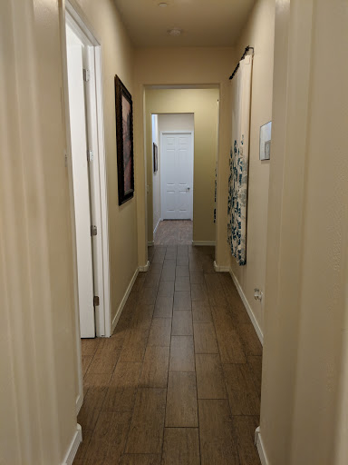 A well-lit hallway leading to a closed door, featuring neutral walls and tiled flooring.