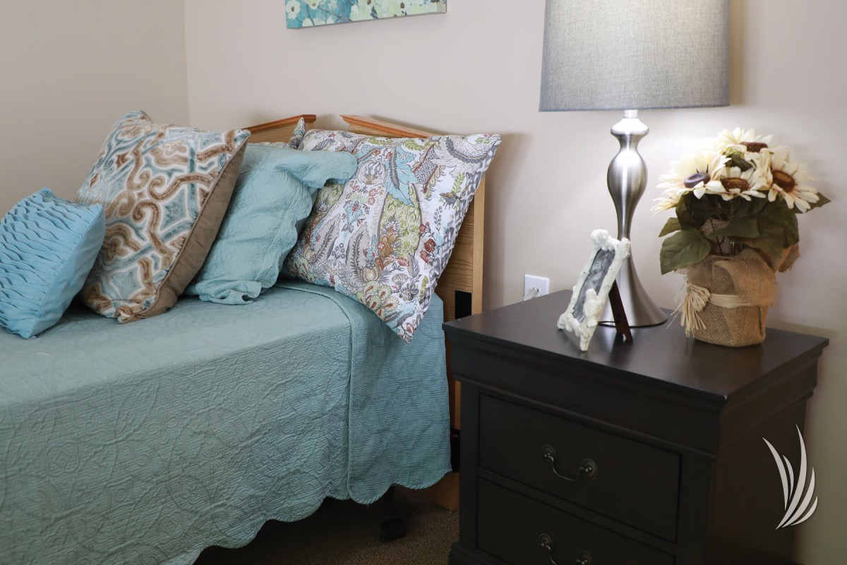 A cozy bedroom corner with a neatly made bed, decorative pillows, and a stylish nightstand lamp.