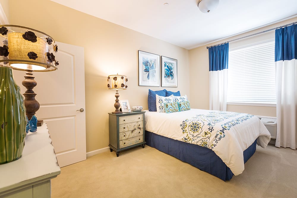 A cozy bedroom with warm tones and blue accents, featuring a bed, nightstand with a lamp, and decorative wall art.