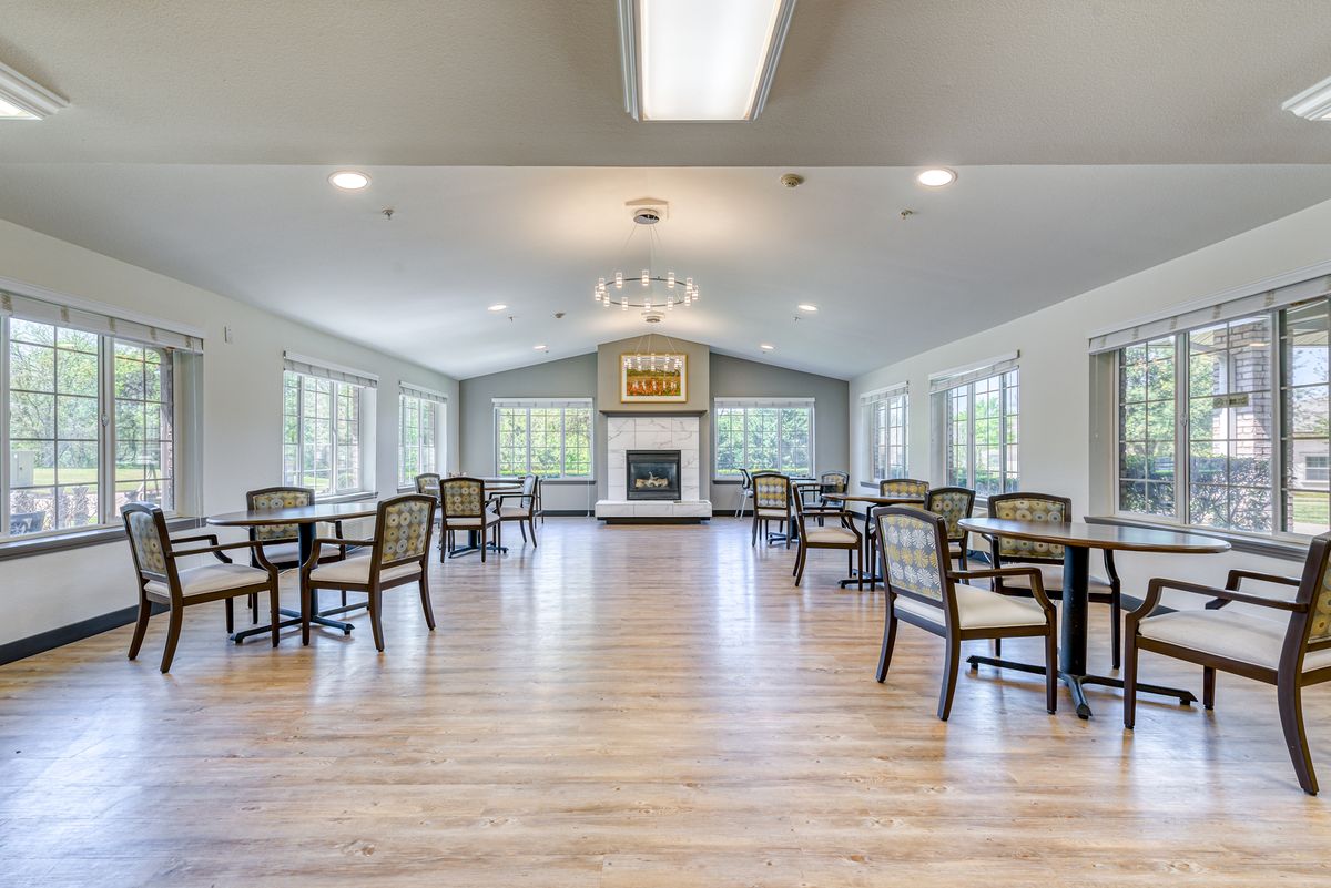 A spacious dining room with multiple tables and chairs, featuring a fireplace and a chandelier.
