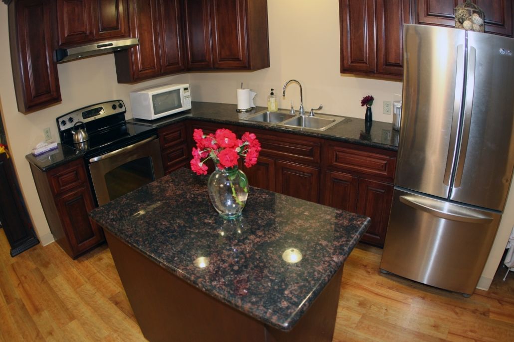 A modern kitchen with granite countertops and wooden cabinets, featuring a centralized island adorned with flowers.