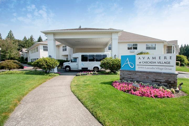 The entrance to a building with a covered driveway and a parked van, surrounded by well-maintained landscaping and signage.