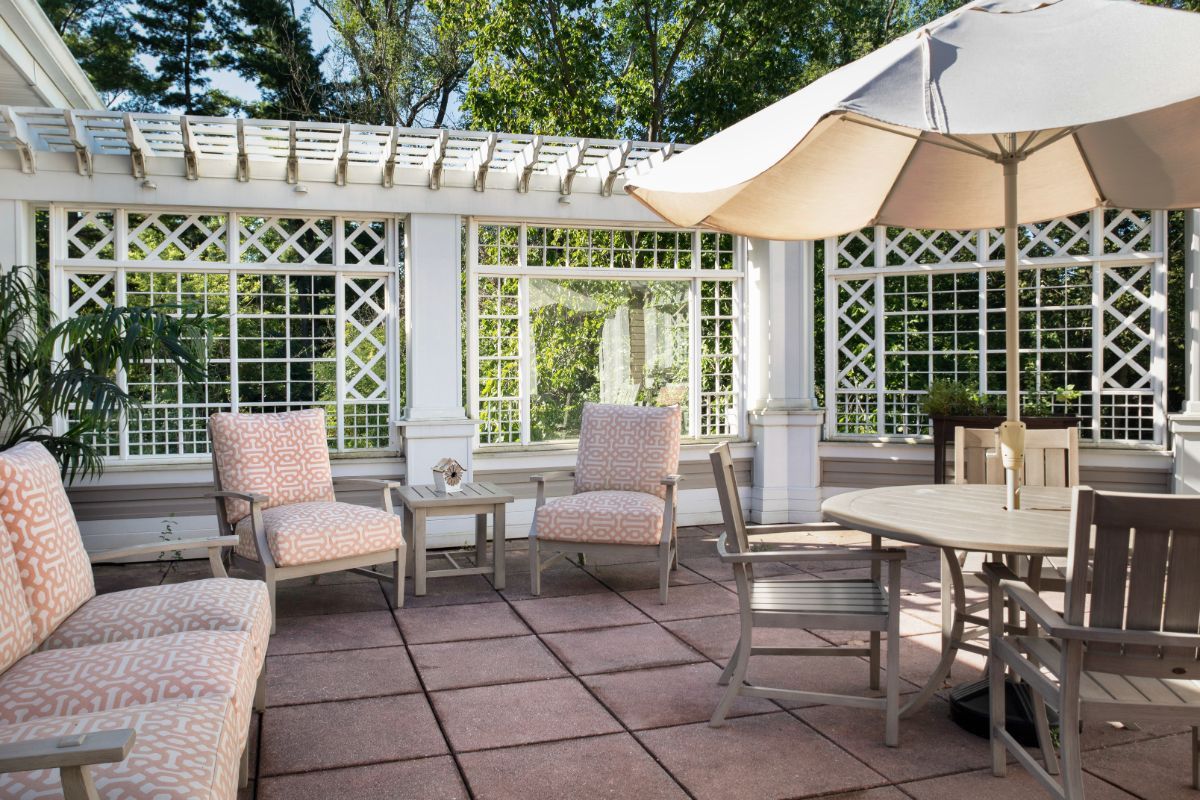 A cozy outdoor patio with comfortable seating under a pergola, featuring a shade umbrella and garden view.