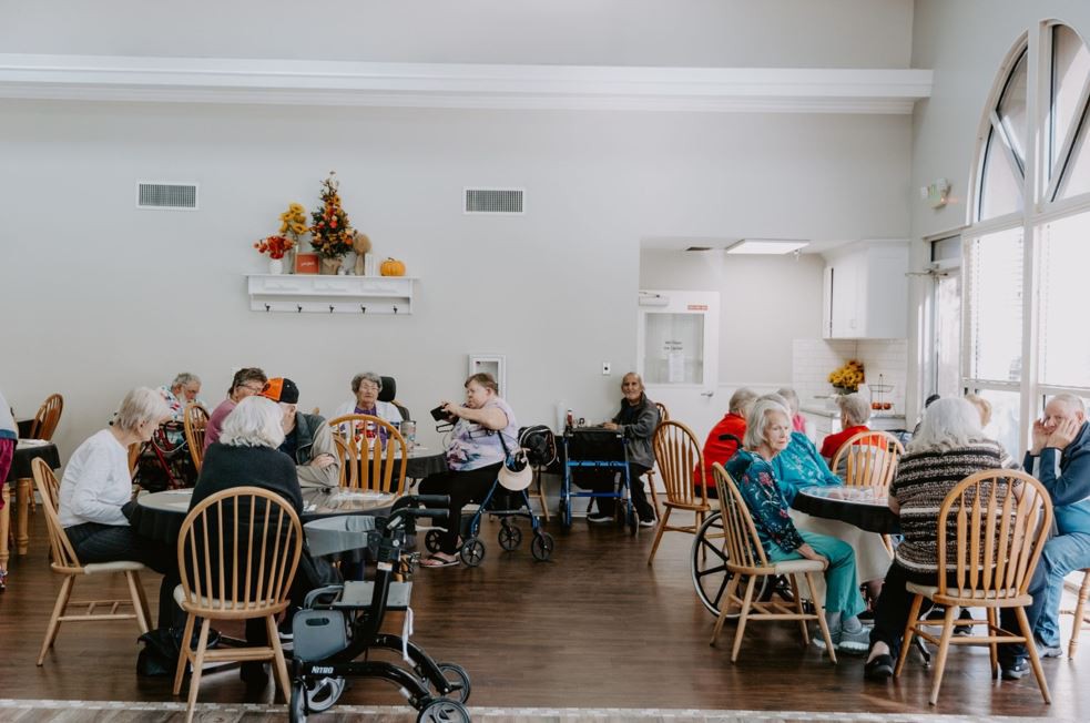 A group of elderly individuals gathered in a nursing home common area, socializing and spending time together.