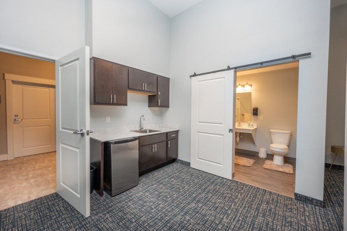 A modern office space featuring a kitchenette and an adjoining bathroom.