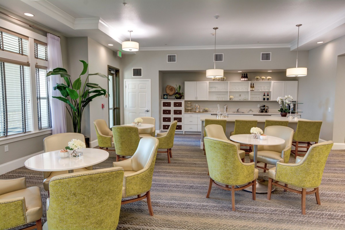 A modern dining area with elegant green chairs and round tables, featuring a stylish kitchen in the background.