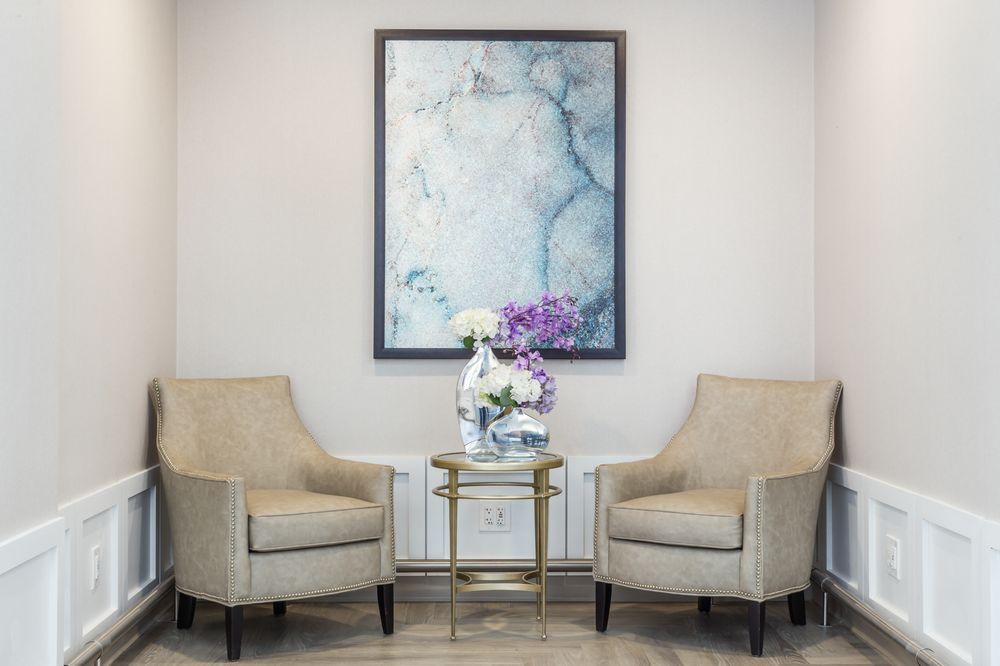 A cozy seating area with two chairs, a small table adorned with flowers, and a framed painting on the wall.